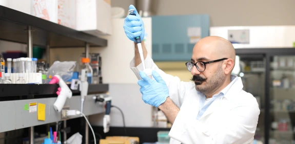 A man in a white lab coat using a dropper.