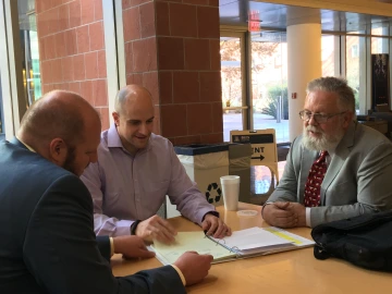 An image of Michael Heien, John Streicher, and Robin Polt seated at a table, talking over notes..